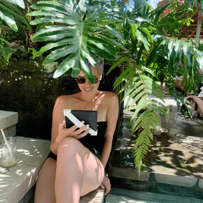 A woman reading Kindle by the pool with the Kindle holder strapsicle white